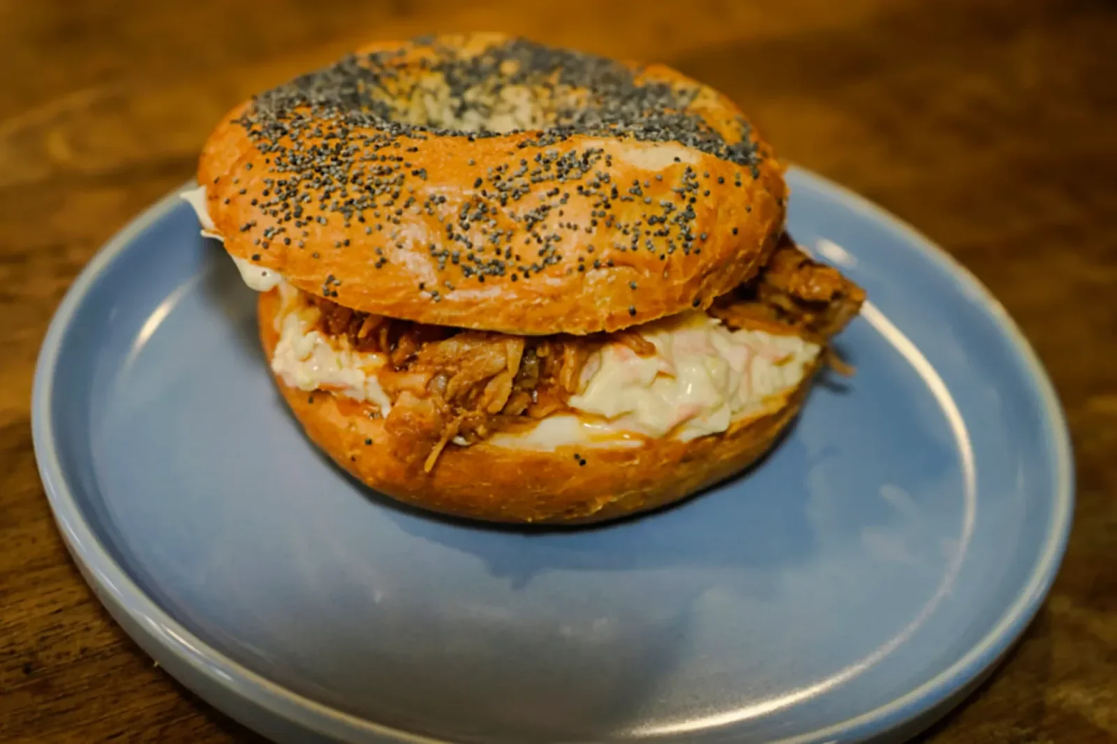 Bagel relleno de pulled pork y ensalada cremosa servido en plato azul en La Nonna Brunch, en el centro de Figueres