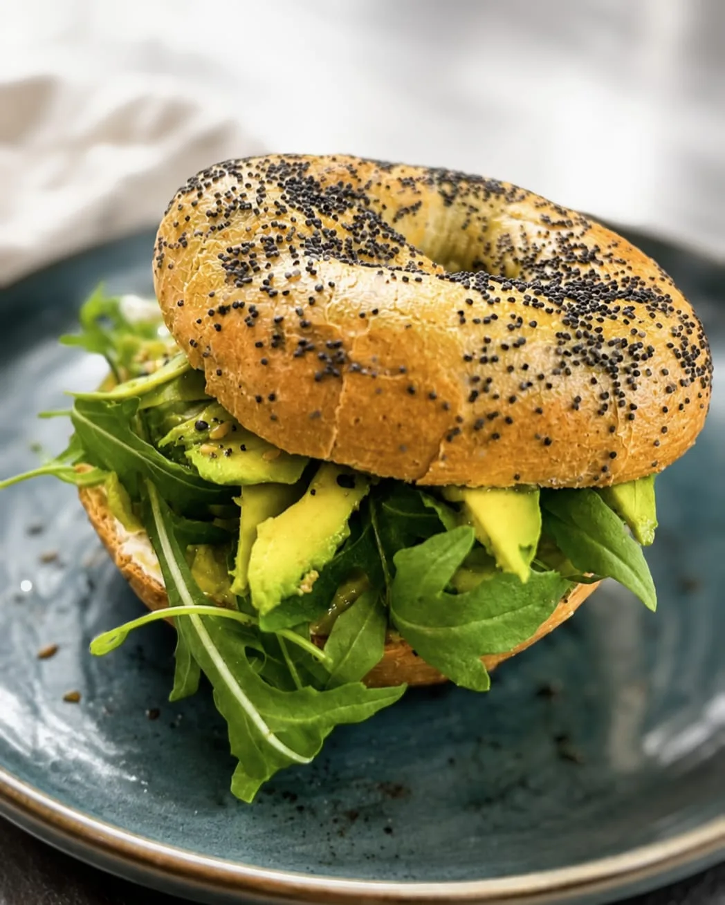 Bagel de aguacate y rúcula sobre plato azul, merienda salada en La Nonna Brunch, en Figueres
