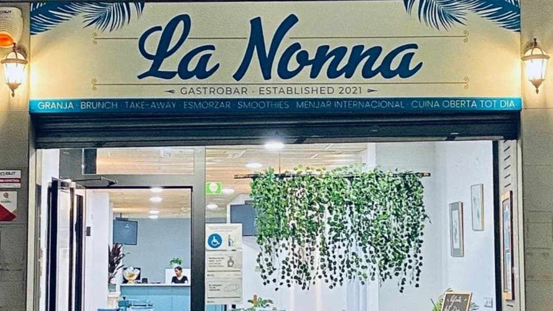 Rincón acogedor con sofá marrón, planta decorativa y neón de café en La Nonna Brunch, en el centro de Figueres