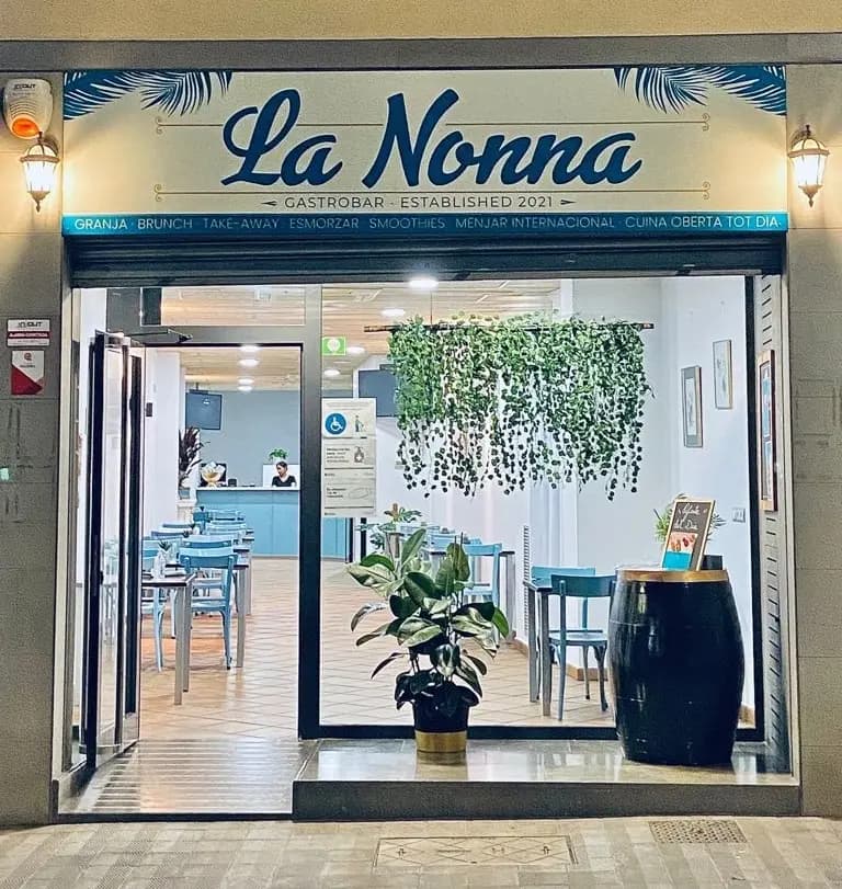Rincón acogedor del interior de La Nonna Brunch en Figueres, con sillón, plantas y decoración cálida en madera y tonos blancos